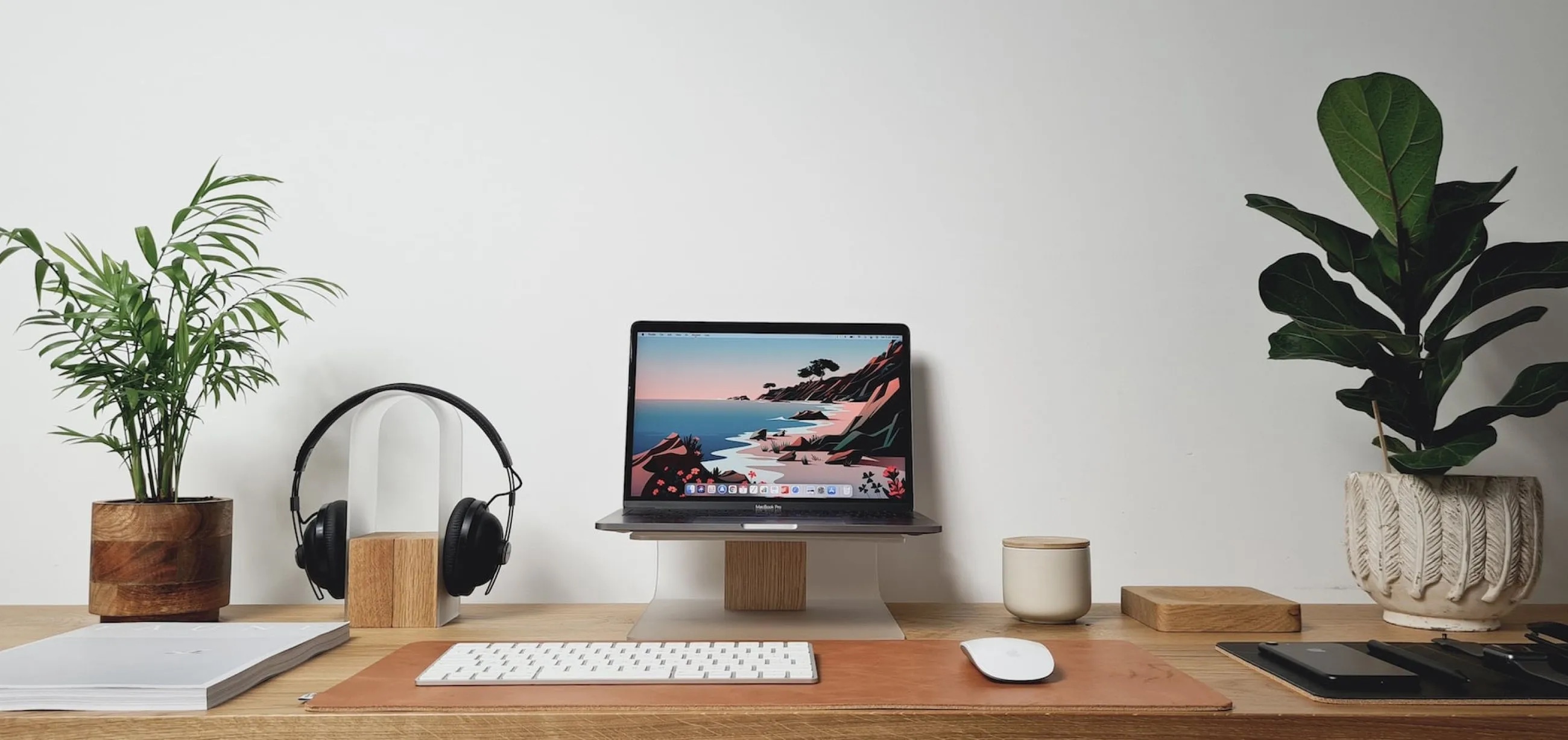 A laptop on a wooden desk between houseplants, headphones, and a keyboard.